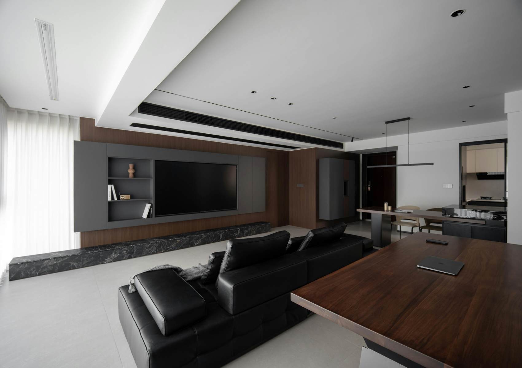 Modern living room with black leather sofas, a timber table and a television set within dark timber cabinetry