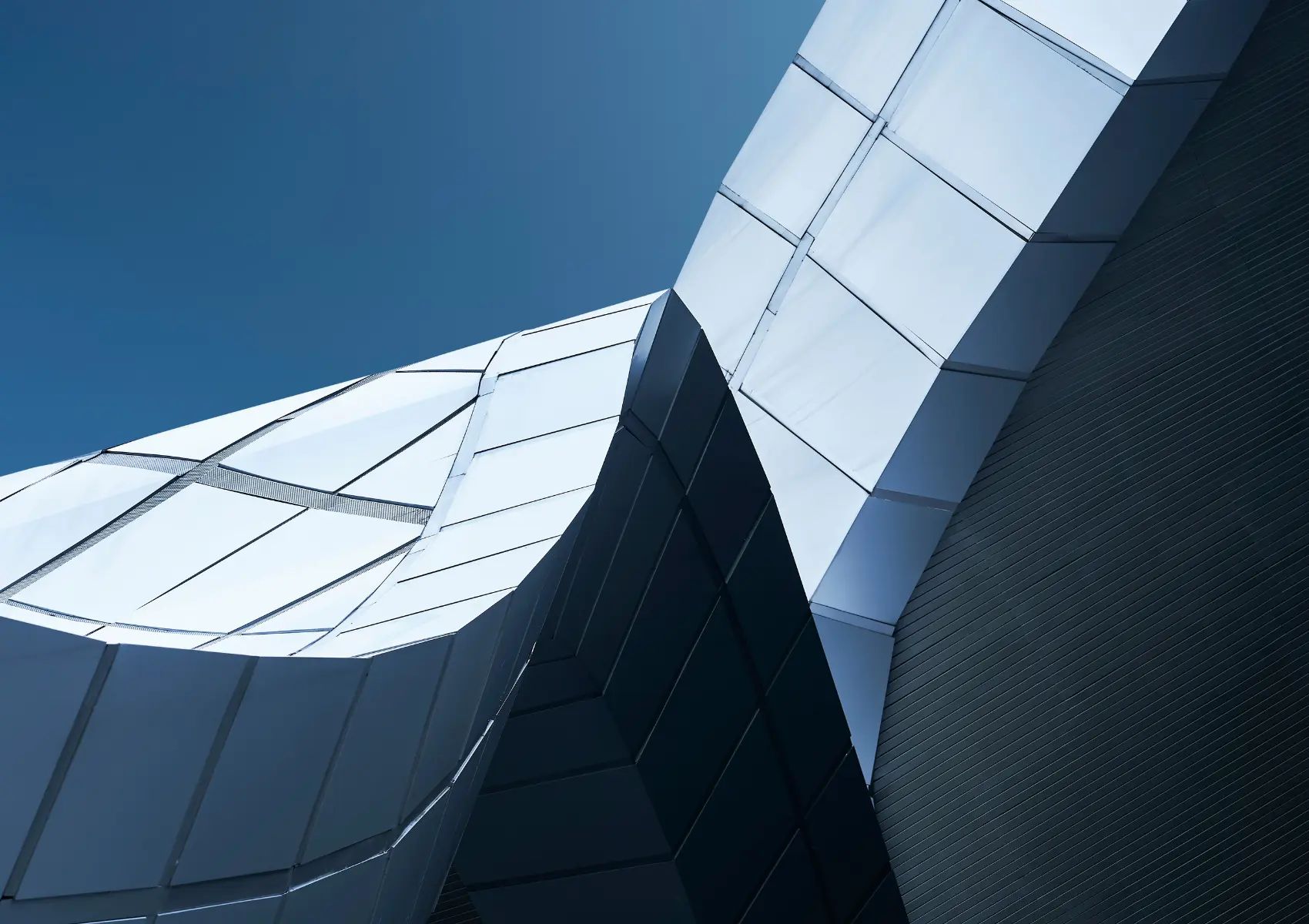 Upward view of angular glazed façades reflecting a clear blue sky